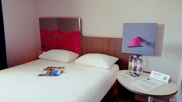 A hotel room with a bed, a small table with a lamp, a water bottle, and a welcome sign.