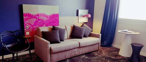 A room with a sofa, a chair, a table, and a large abstract painting on the wall.