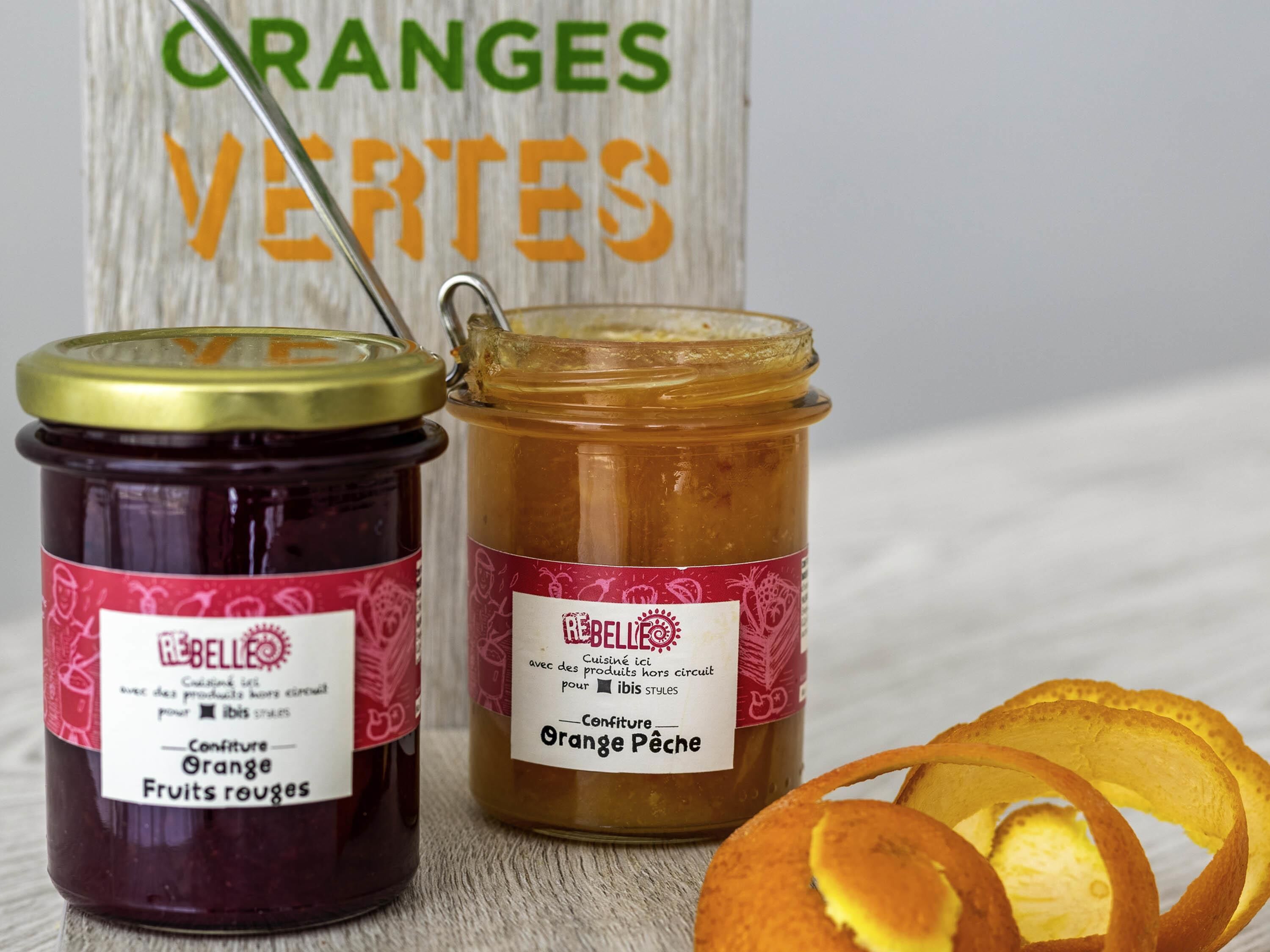 Two jars of fruit preserves with labels, one red and one orange, and a wooden sign with 'CRANGES VERTES' in the background.
