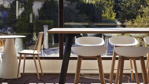Un comedor con mesa y sillas, vista a un jardín por una ventana, y un edificio al fondo.