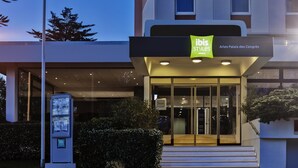 Una entrada de hotel moderna con puerta de vidrio, un letrero que dice 'ibis Styles Hotel' y un quiosco informativo digital.