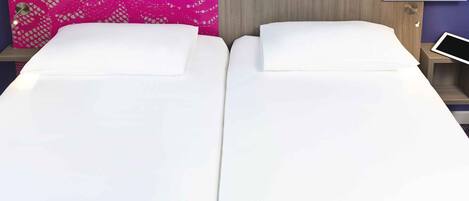 A double bed with white linens, a wooden headboard, and a pink lace panel on the wall.