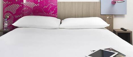 Una cama bien hecha con sábanas blancas, un cabecero decorativo rosa, una mesita de noche con lámpara y una lámpara de pared.