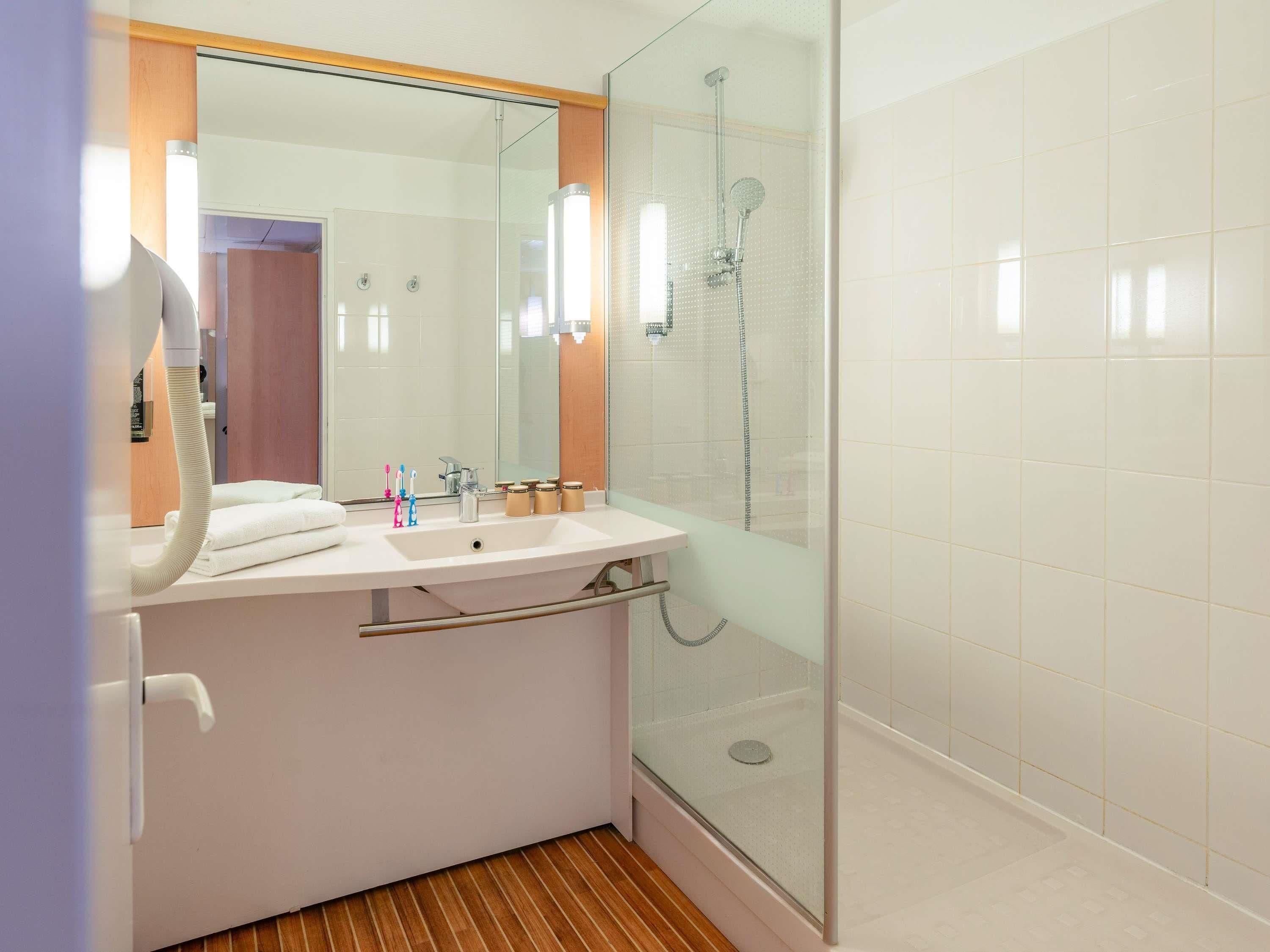 A modern bathroom with a glass-enclosed shower, a white sink with a mirror, and a wooden floor.