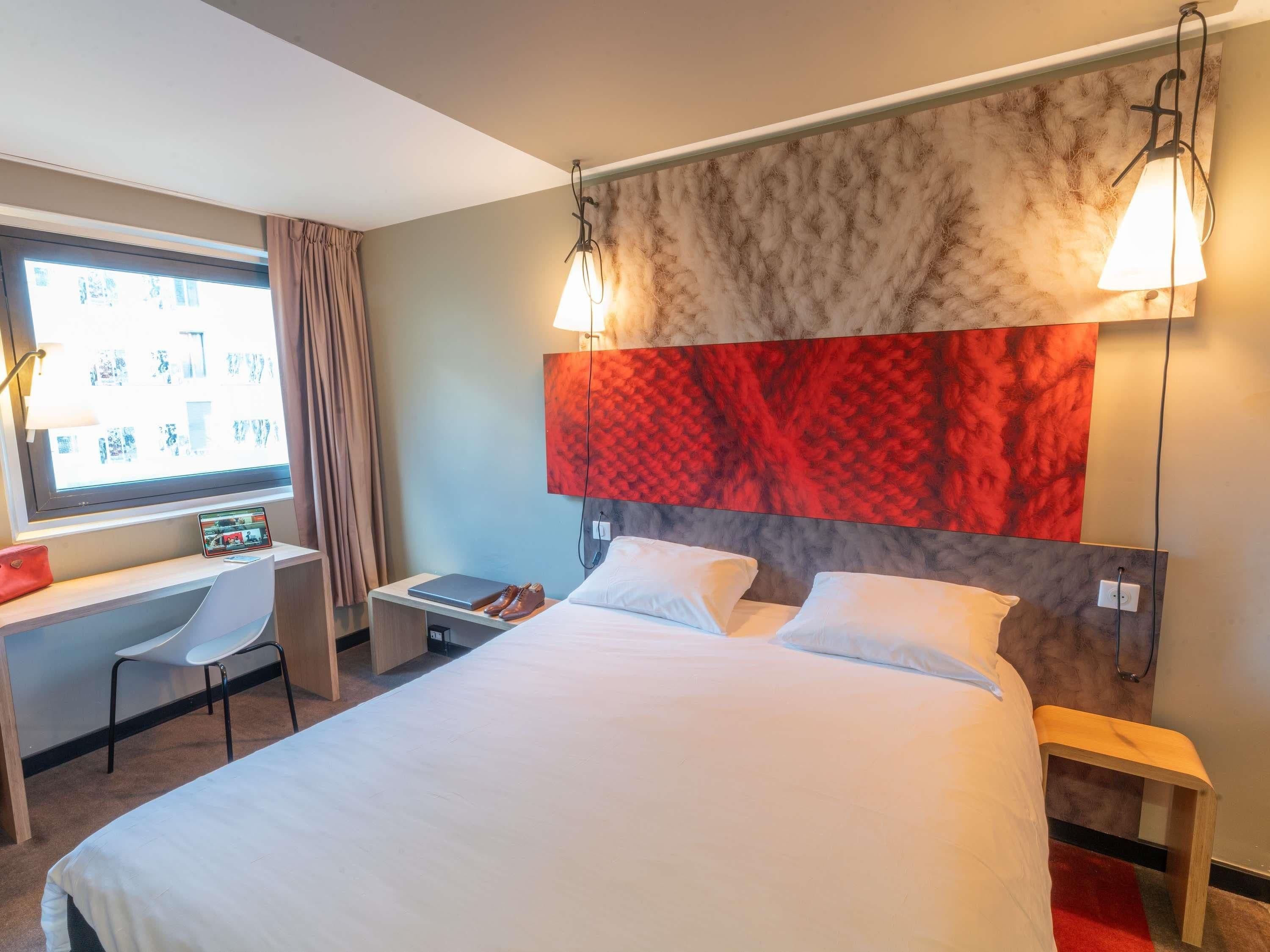 Een hotelkamer met een bed, een bureau met een laptop, een stoel en een groot raam.