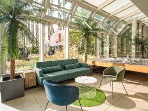 Un espacio interior moderno con un sofá verde, dos sillones, una mesa de centro y una exposición de una maqueta de ciudad.