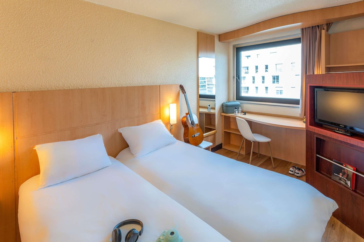 Une chambre d’hôtel avec deux lits, un bureau, une télévision et une fenêtre donnant sur des immeubles.