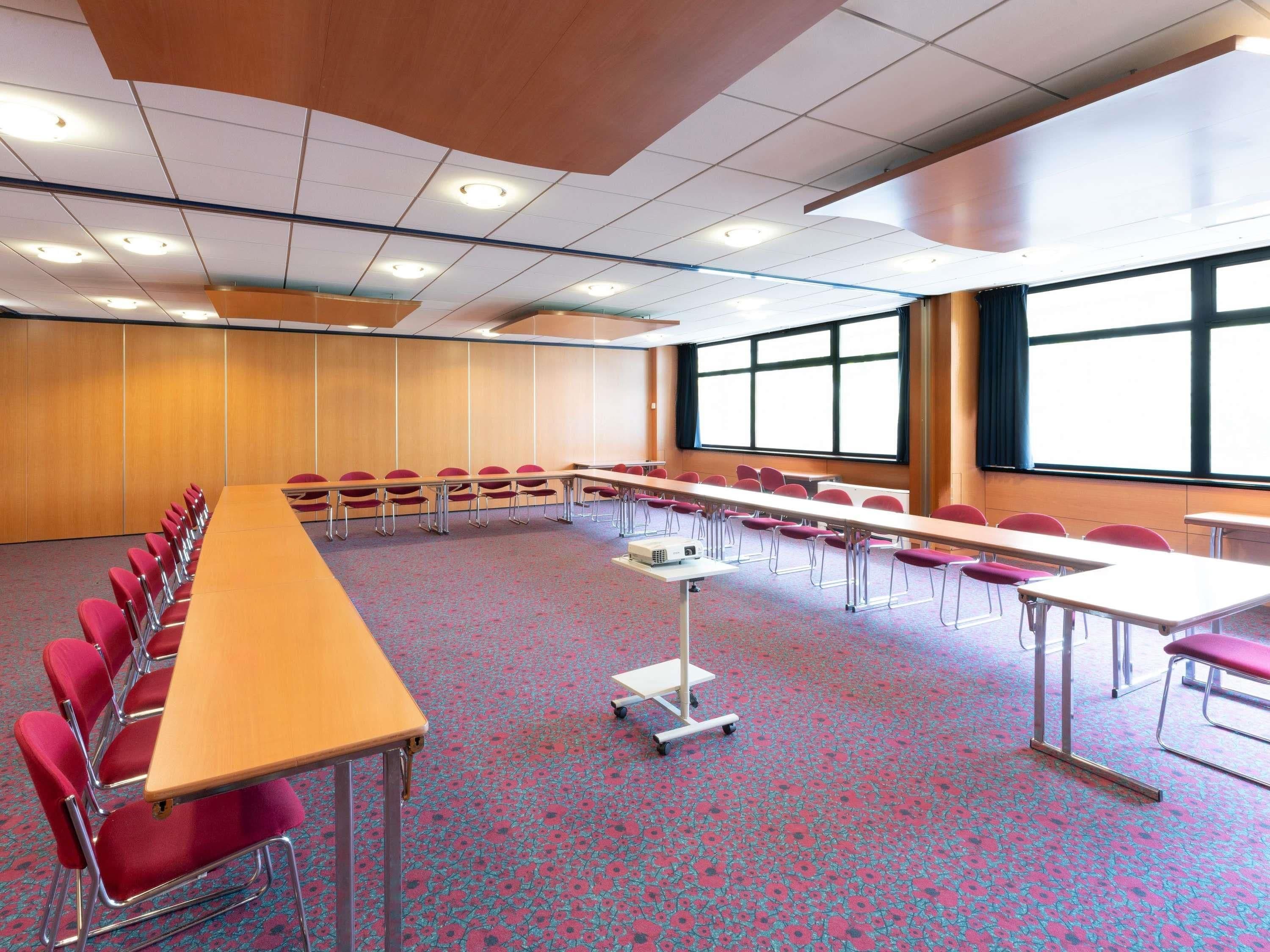 A conference room with a long table, rows of chairs, a projector, and large windows.
