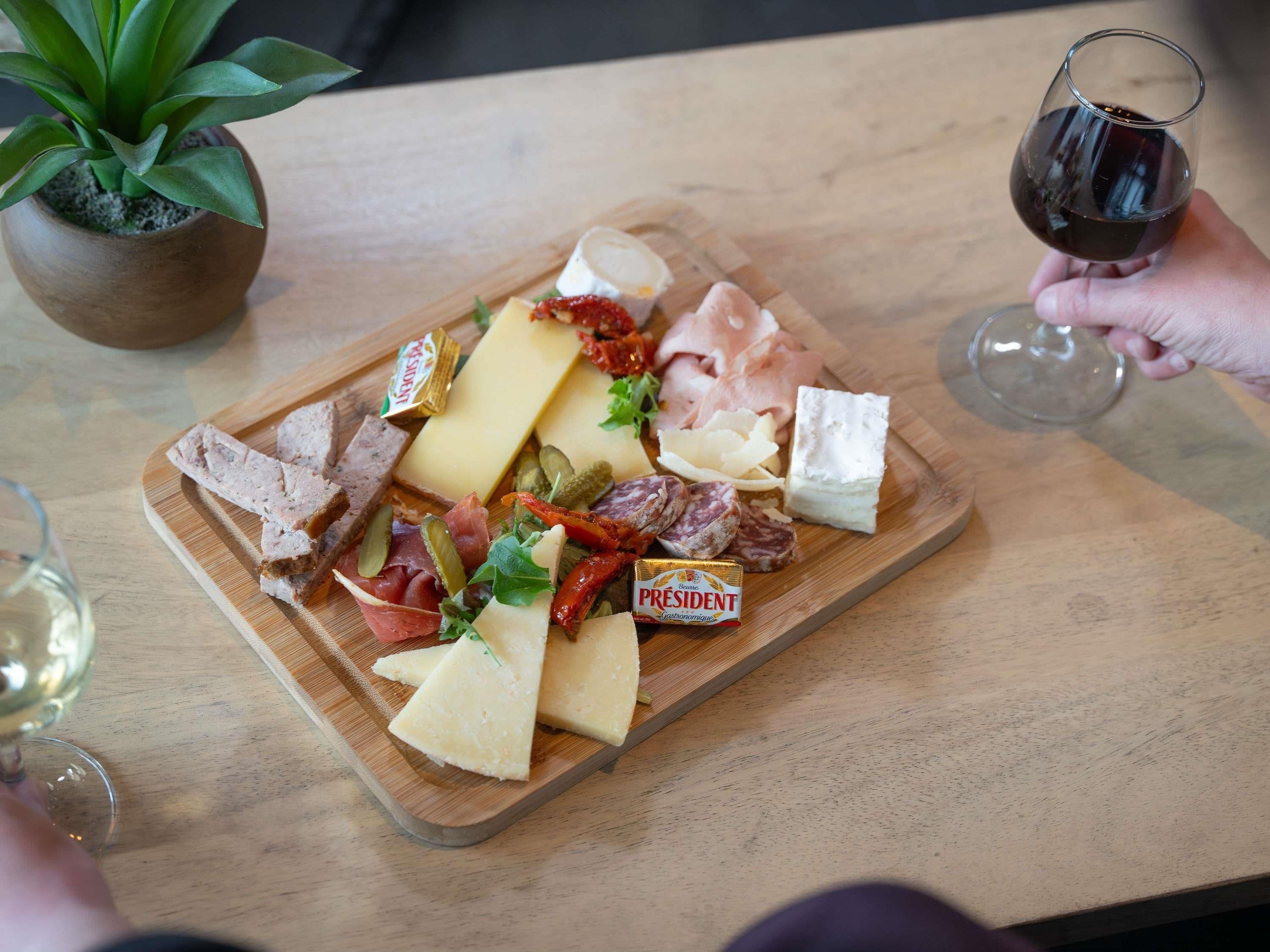 A wooden board with various cheeses, meats, and pickles.