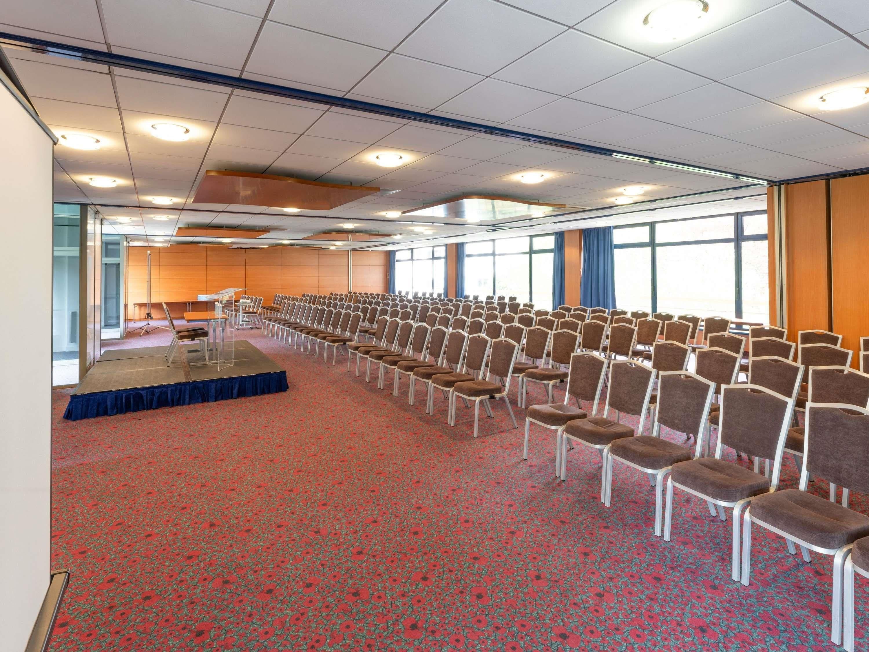 A conference room with rows of chairs, a stage, and large windows.