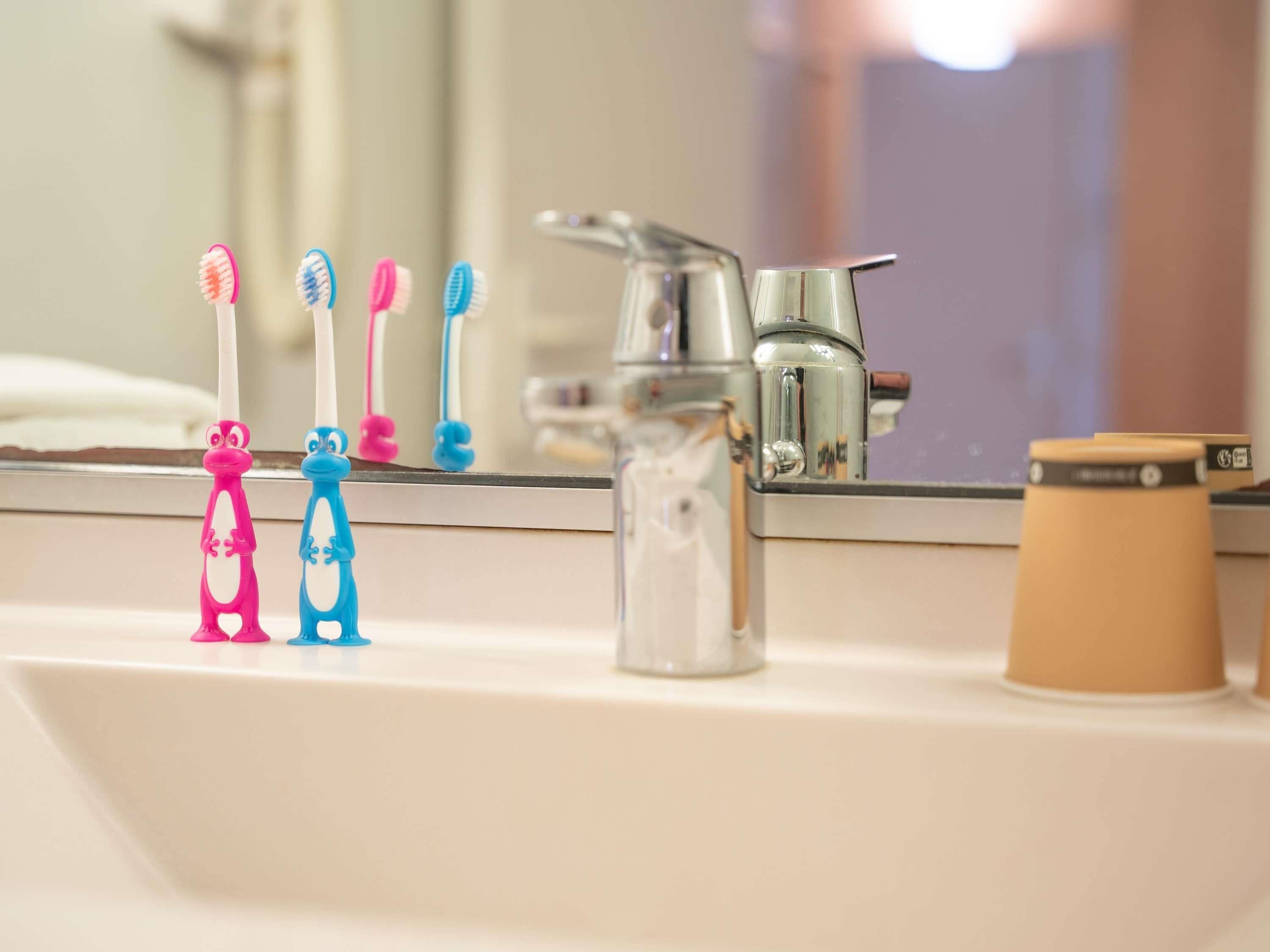 A bathroom sink with a mirror above it, a faucet, and three toothbrushes with animal designs.