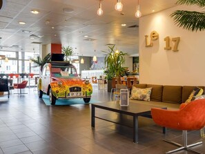 Un moderno vestíbulo de hotel con un coche antiguo, una recepción y un área de descanso.