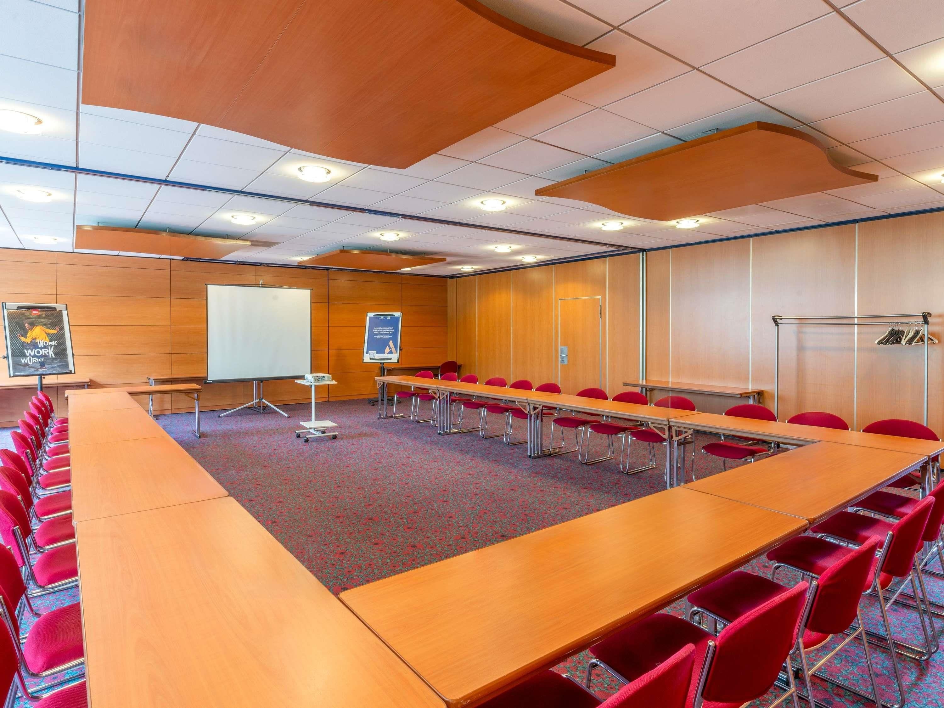 A conference room with a long table, red chairs, a whiteboard, and a projector.