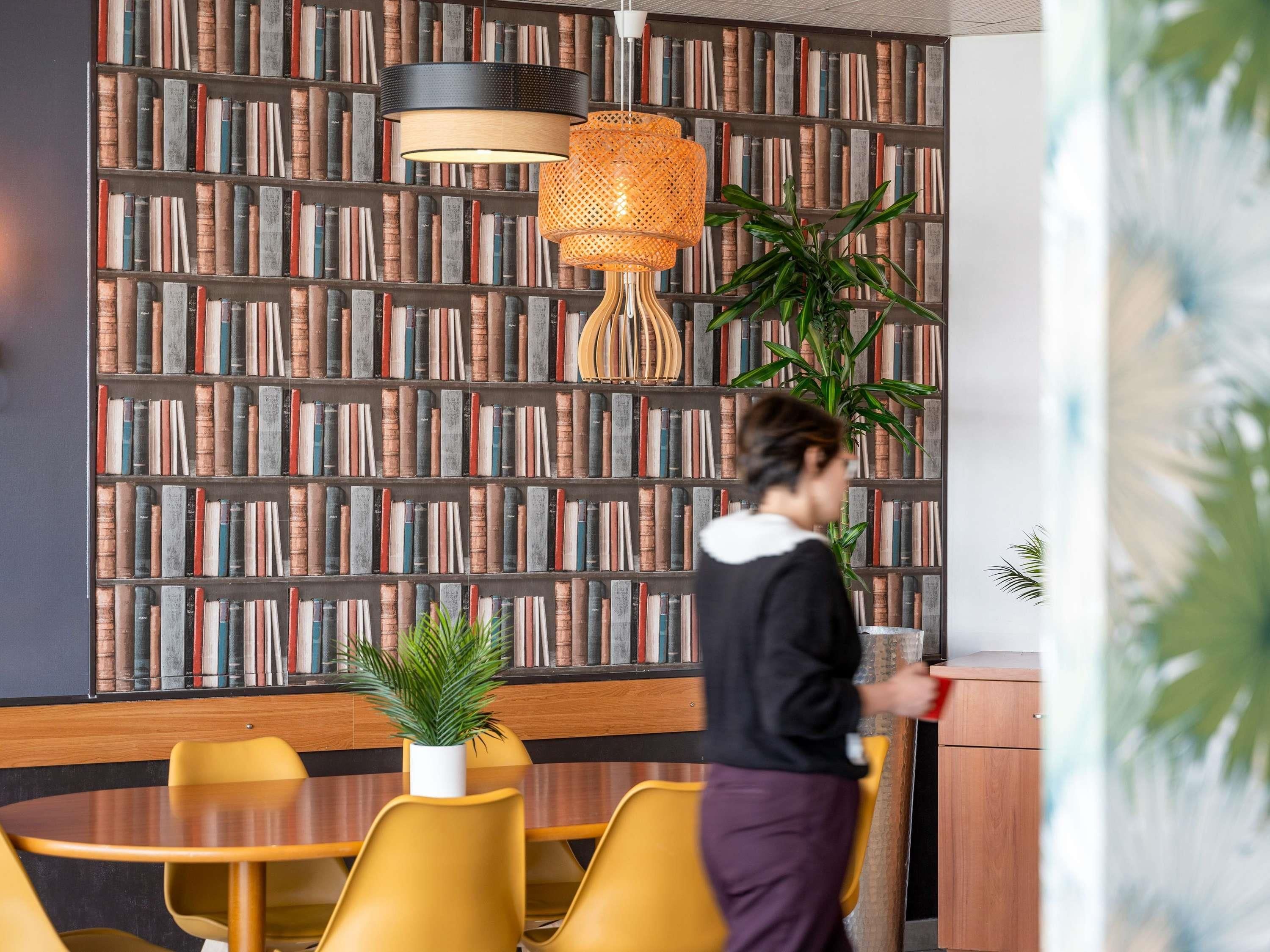 A room with a bookshelf, a round table, yellow chairs, and a potted plant.