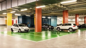 Un parking à plusieurs niveaux avec un revêtement de sol vert et blanc, des piliers orange et des voitures garées dans des emplacements prévus à cet effet.