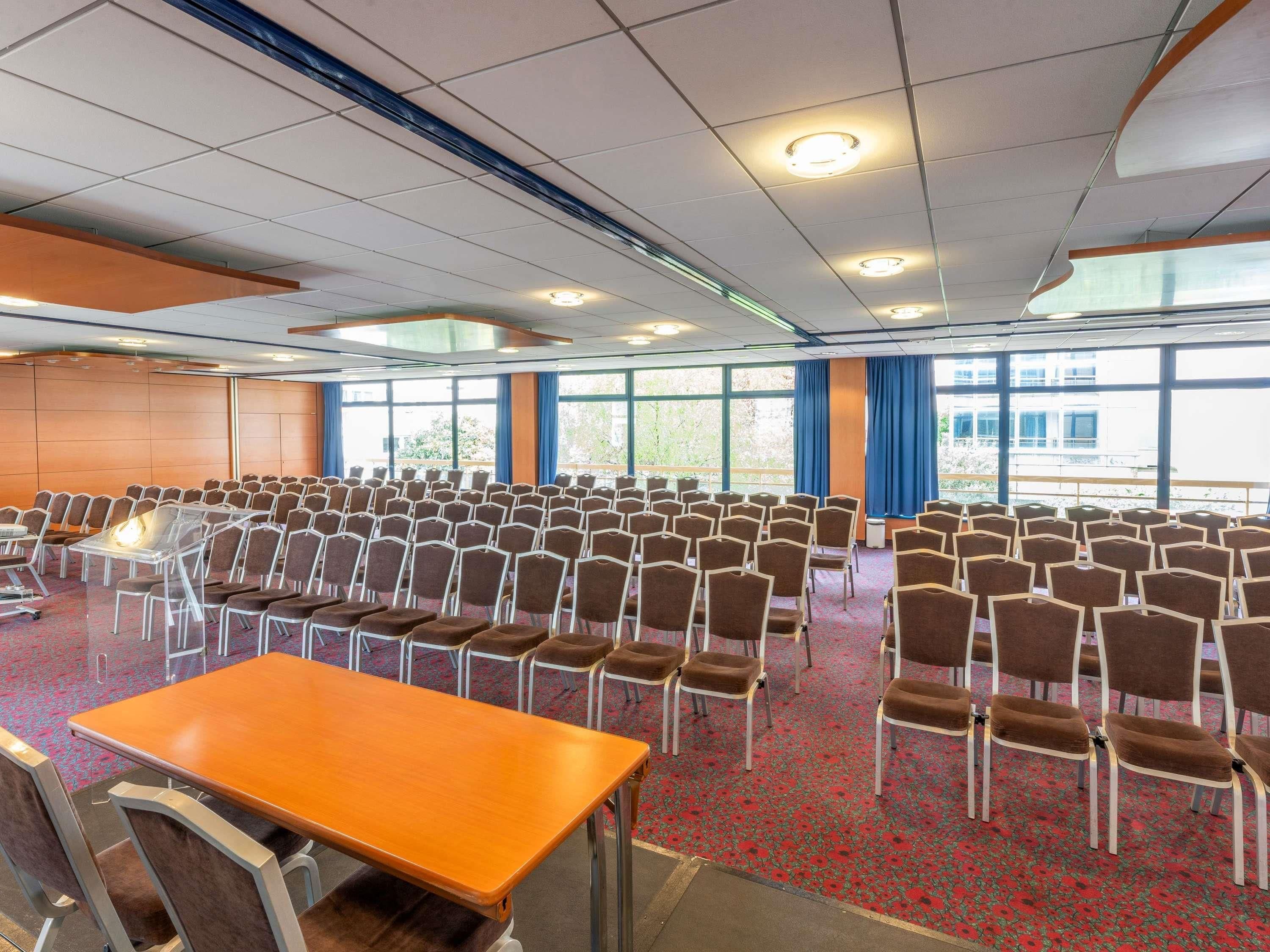 A conference room with rows of chairs, a wooden table, and large windows.