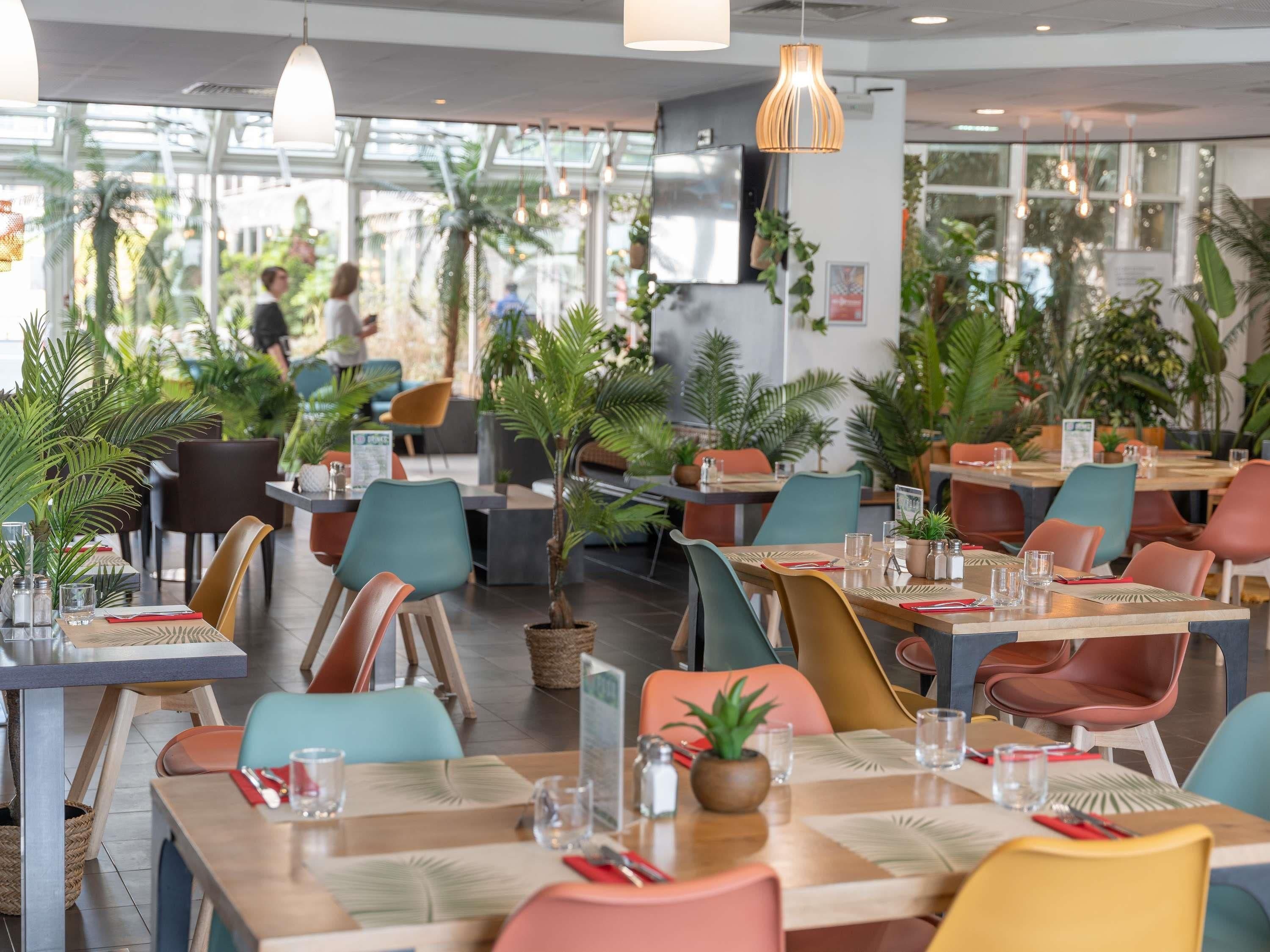 Un restaurant moderne, agrémenté de plantes d’intérieur, de tables en bois et de chaises colorées.
