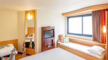 Una habitación de hotel con cama, televisión, ventana con cortinas, un osito de peluche y un llama de peluche.