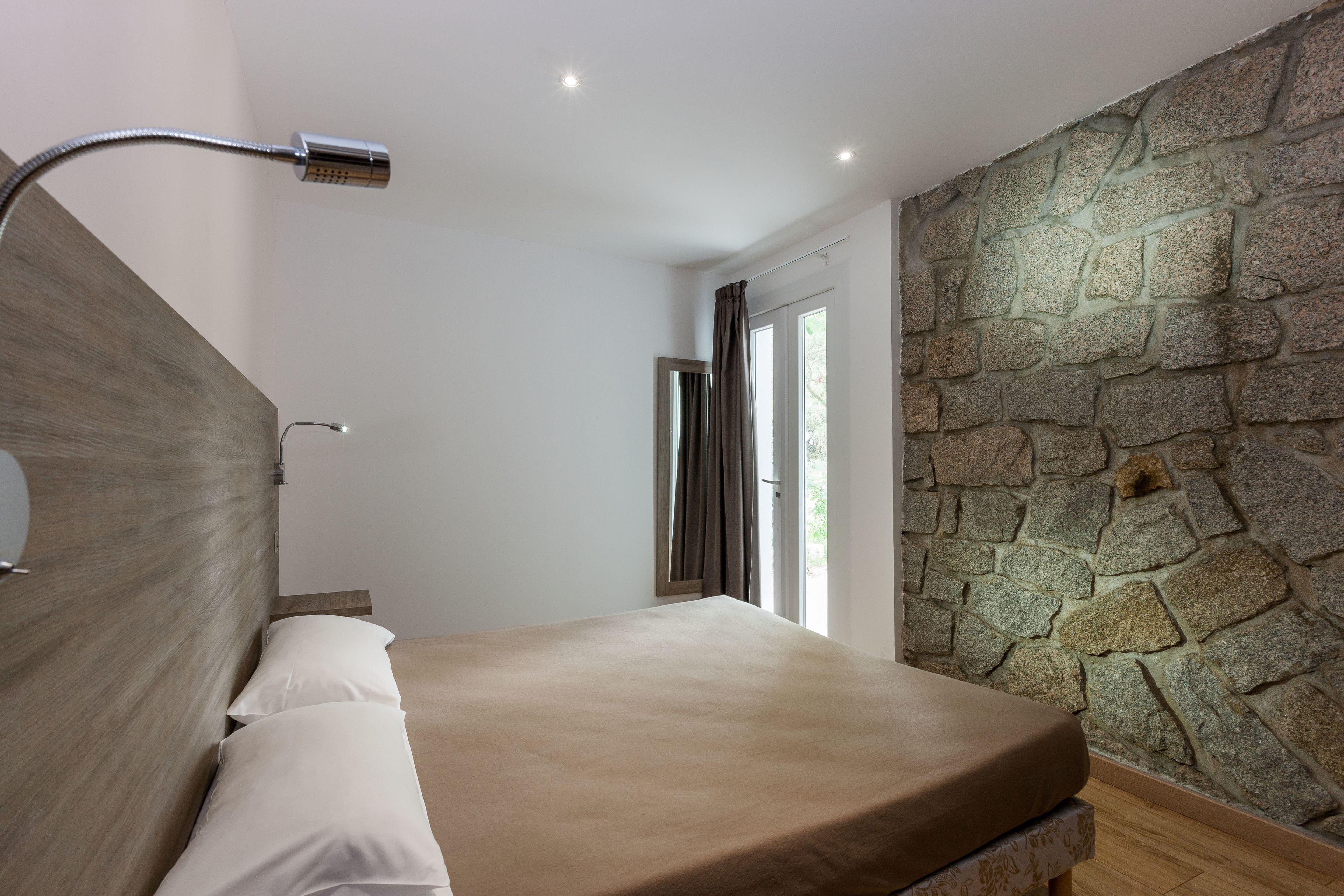 Une chambre avec un mur en pierre, un lit avec un matelas beige et une pomme de douche.