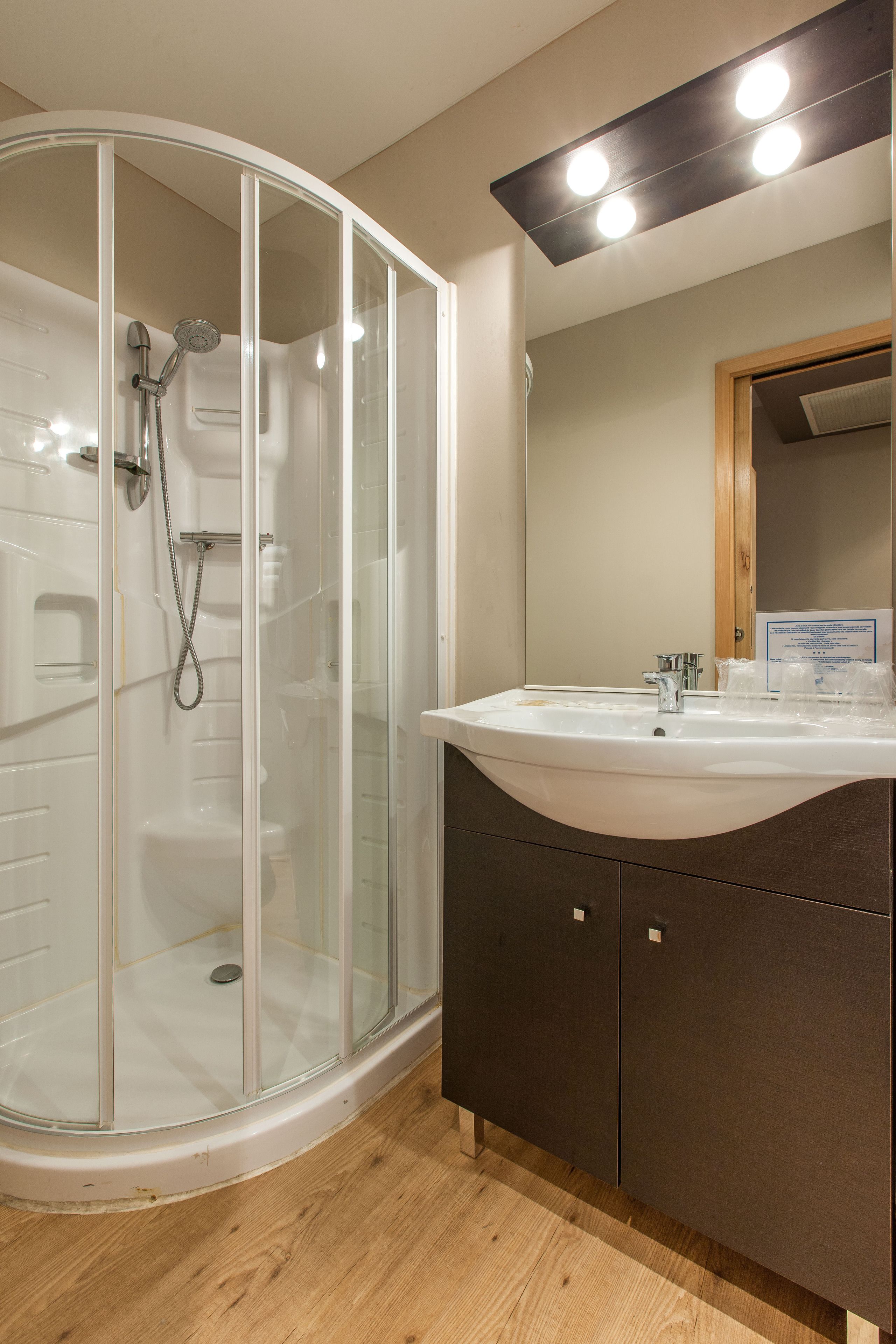 Une salle de bain avec une douche à parois de verre, un lavabo avec un miroir au-dessus et des meubles en bois en dessous.