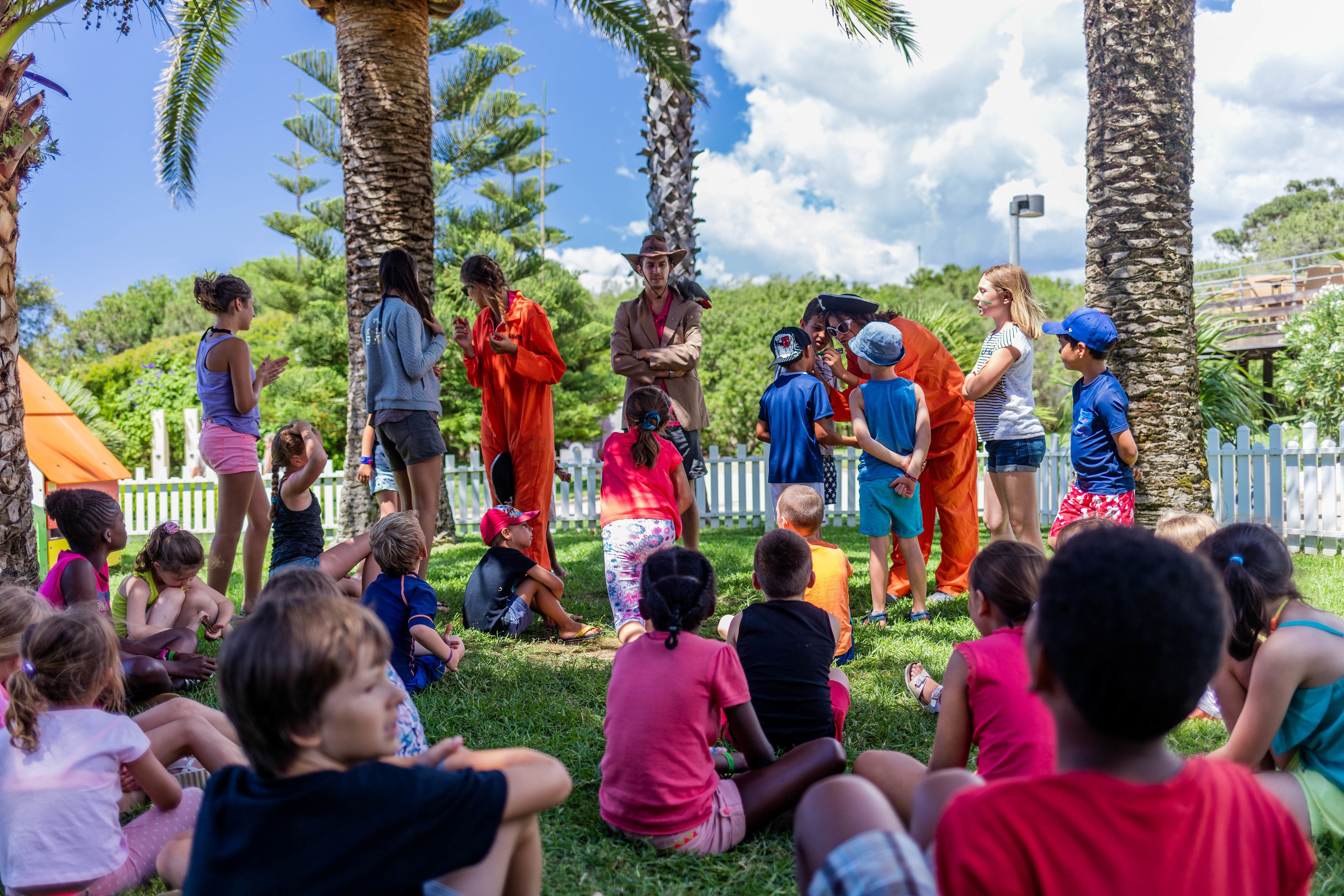 A group of children sitting on grass, with adults standing behind them.