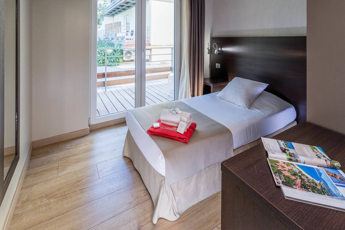 A hotel room with a bed, a desk, and a large window.