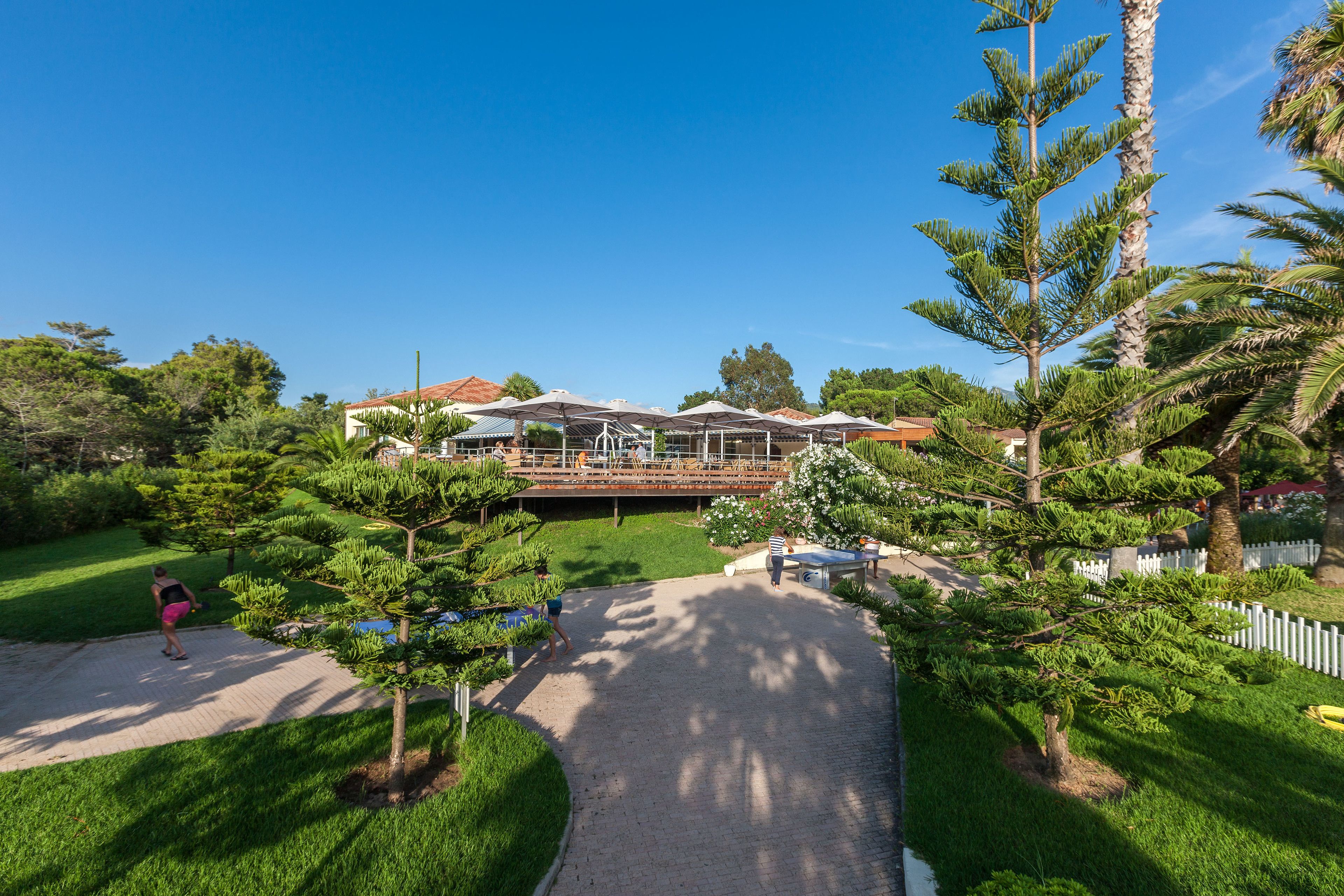 A residential property with a paved driveway, a covered outdoor seating area, and a well-maintained lawn.