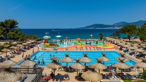 Zona de piscina en un resort, con tobogán de agua, sillas de descanso y sombrillas.