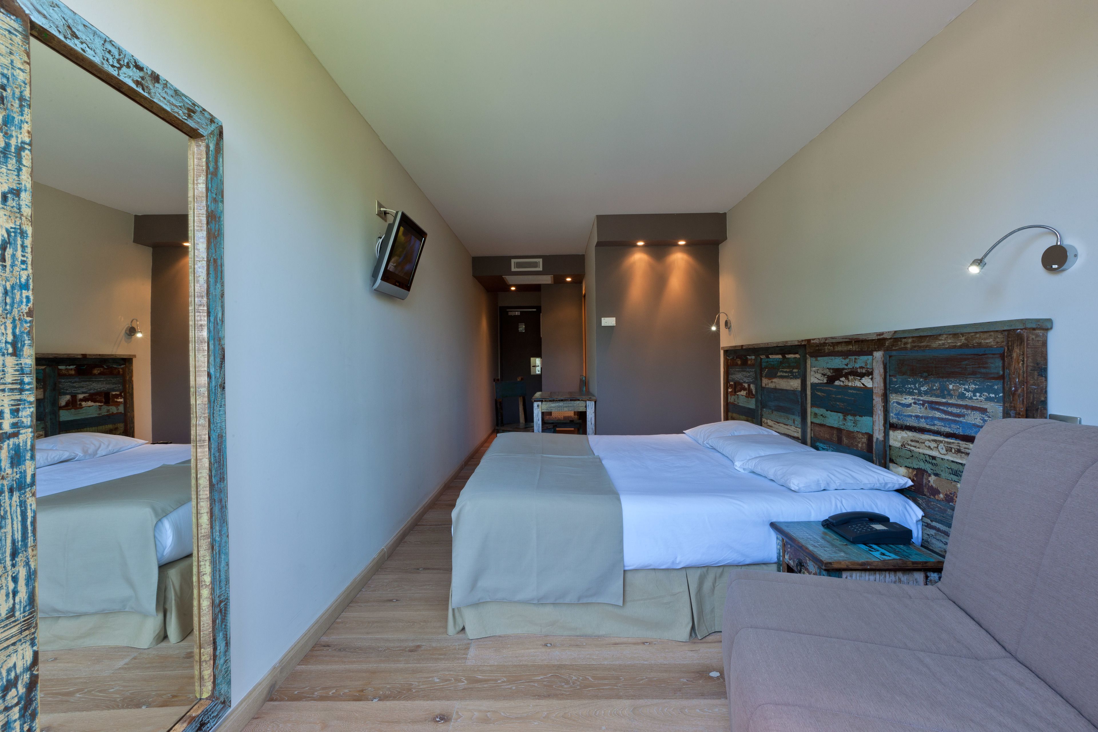 Habitación de hotel con dos camas, un espejo grande, cabecera de madera, una mesita con un teléfono y una lámpara fijada a la pared.