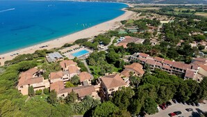 Vista aérea de una zona residencial costera con playa, piscina y villas.