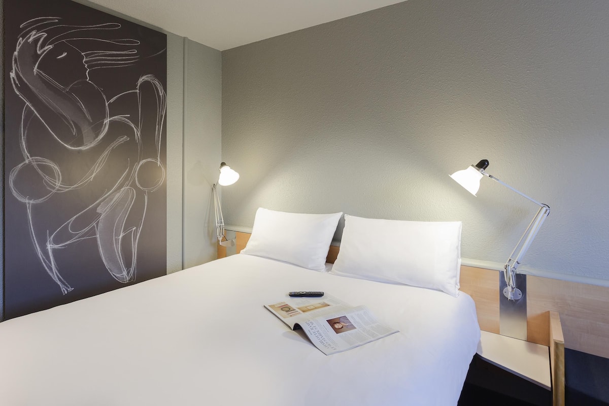 Ein Hotelzimmer mit einem großen Bett, zwei Nachttischlampen, einem Wandbild und einer Zeitschrift auf dem Bett.