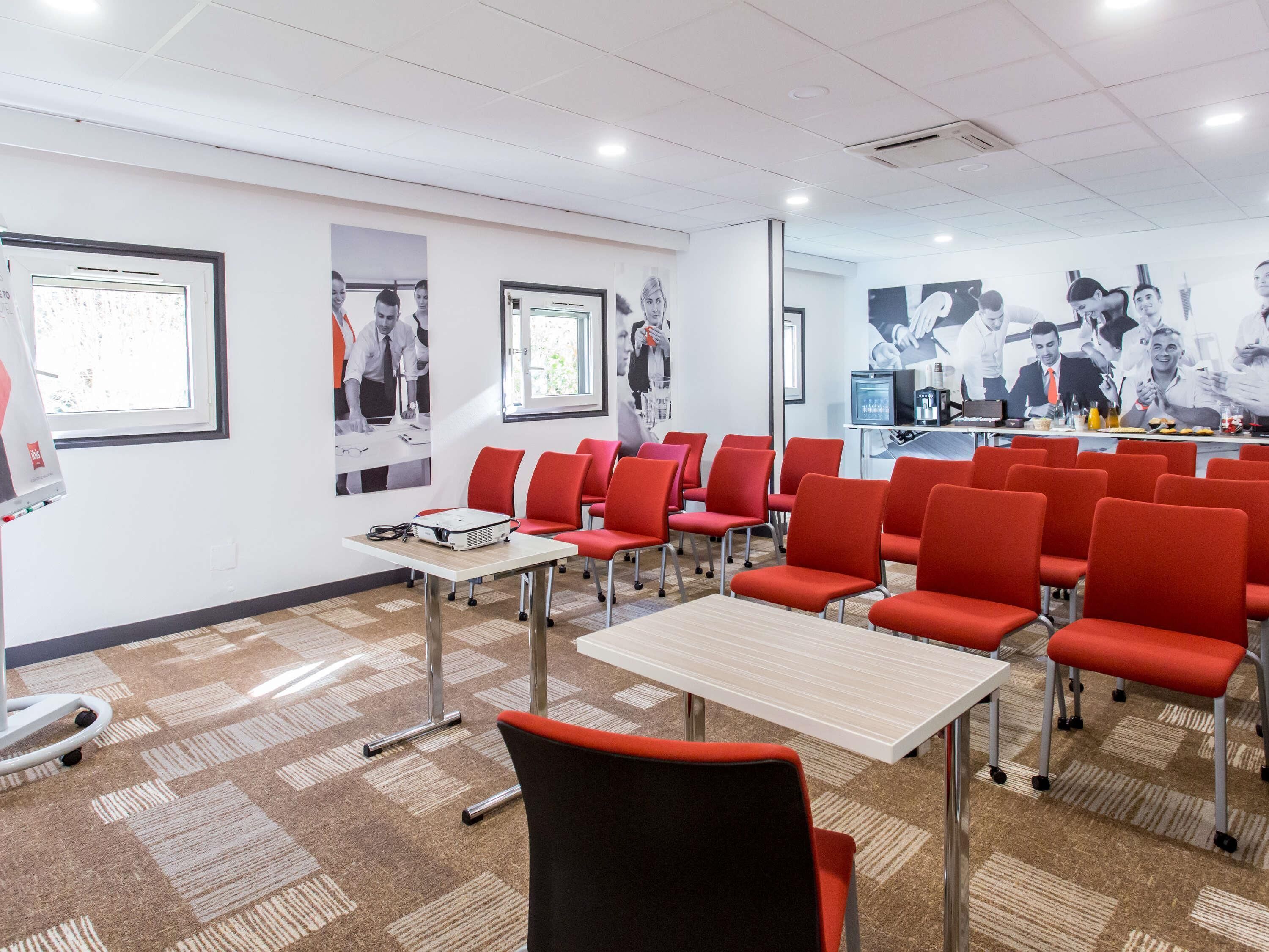 A conference room with red chairs, a projector on a table, and posters on the walls.