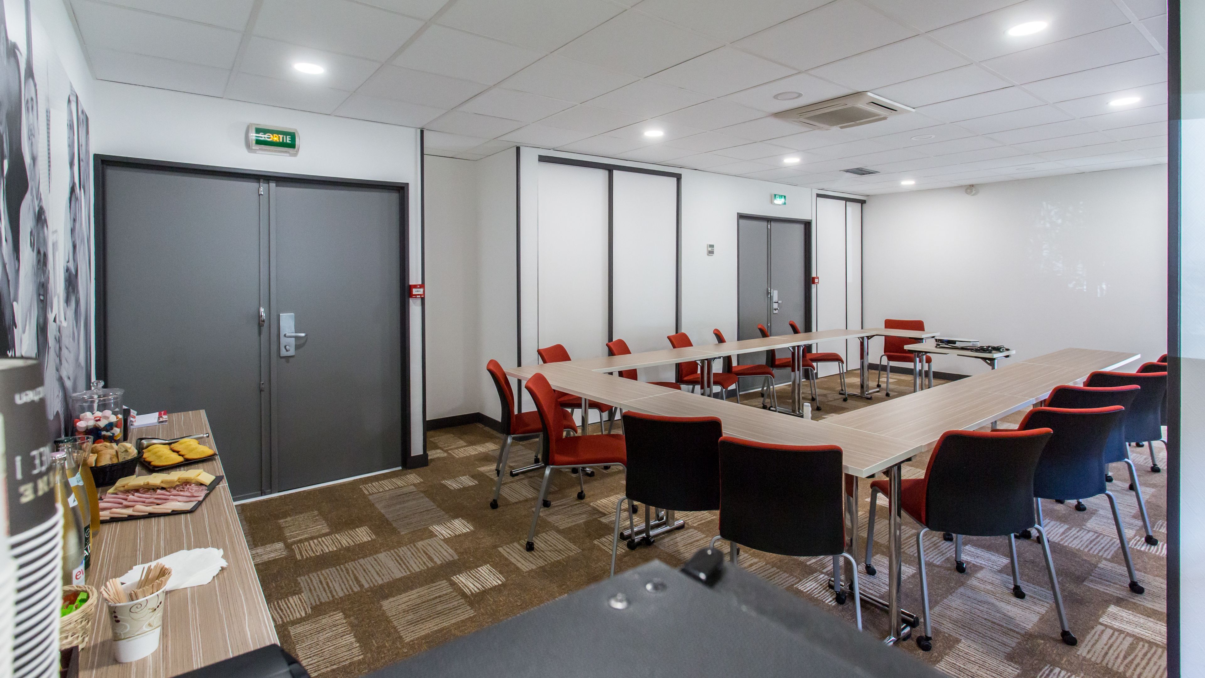 A conference room with a long table, red and black chairs, and a carpeted floor.
