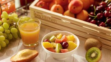 A breakfast setting with a bowl of fruit, a glass of orange juice, and a variety of fresh fruits in the background.