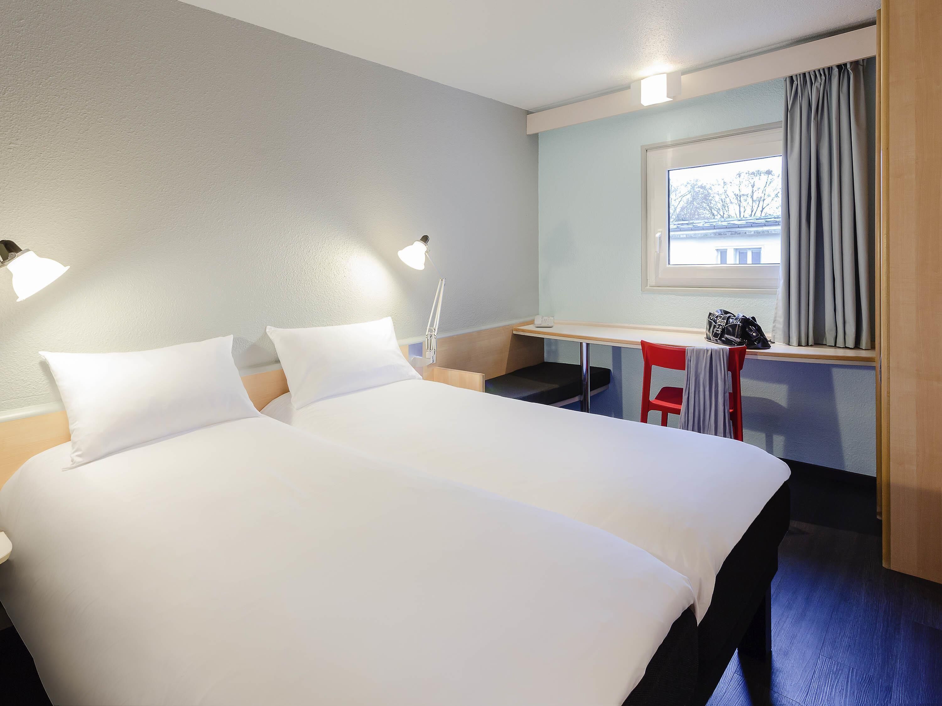 Habitación de hotel con una cama grande, lámparas de noche, un escritorio pequeño, una silla y una ventana con cortinas.