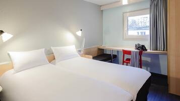 A hotel room with a large bed, bedside lamps, a small desk, a chair, and a window with curtains.