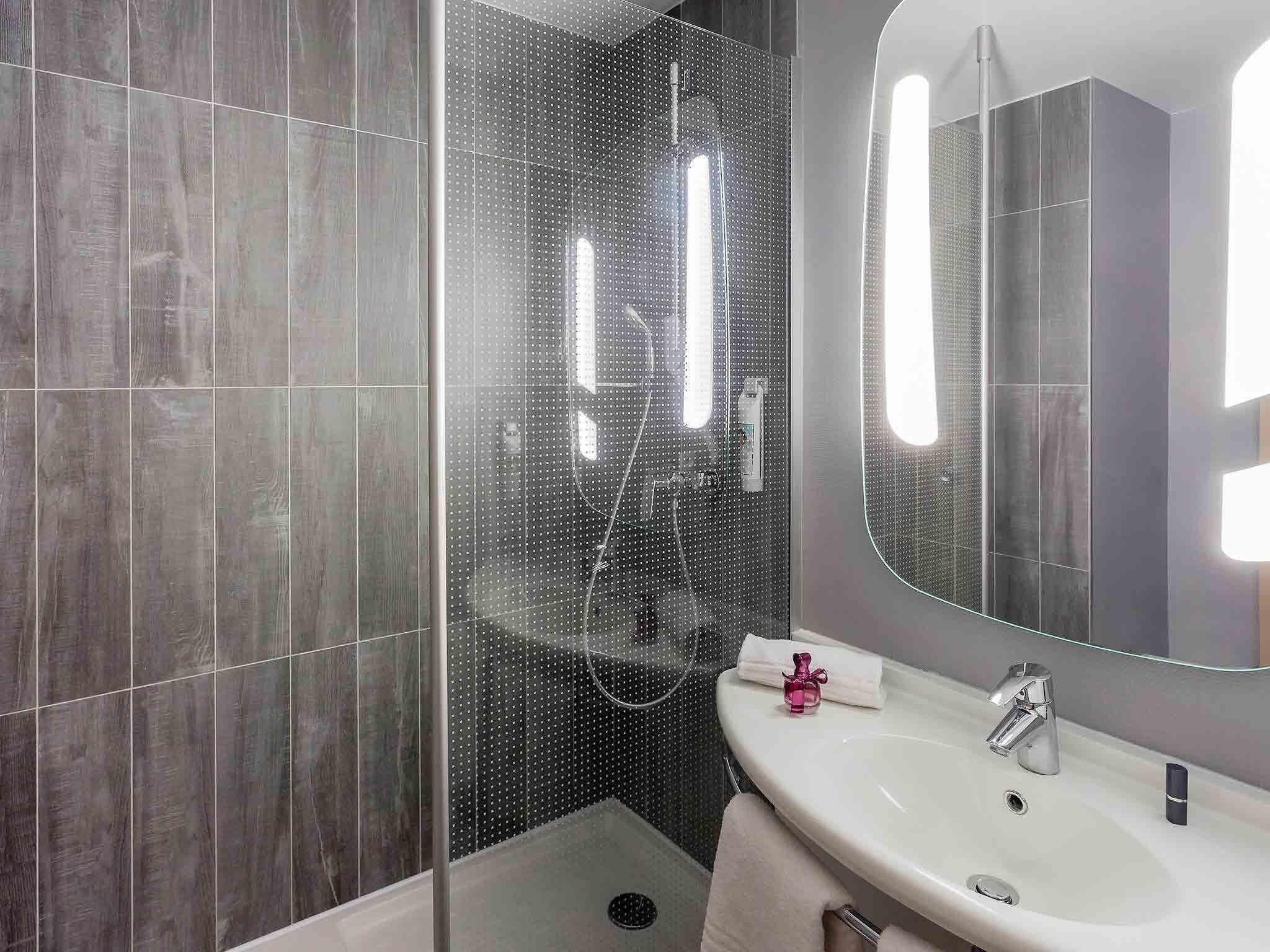 Een moderne badkamer met een glazen douchecabine, een grote spiegel en een witte wasbak.