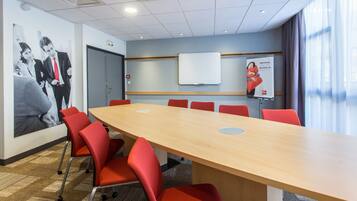 A conference room with a long table, red chairs, a whiteboard, and a poster on the wall.