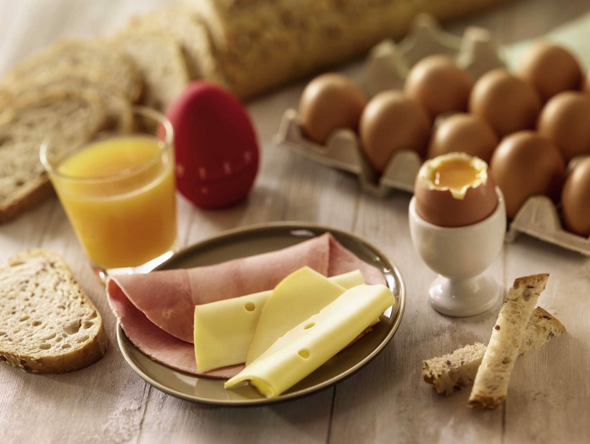 A breakfast setting with bread, eggs, cheese, and a glass of orange juice on a wooden table.