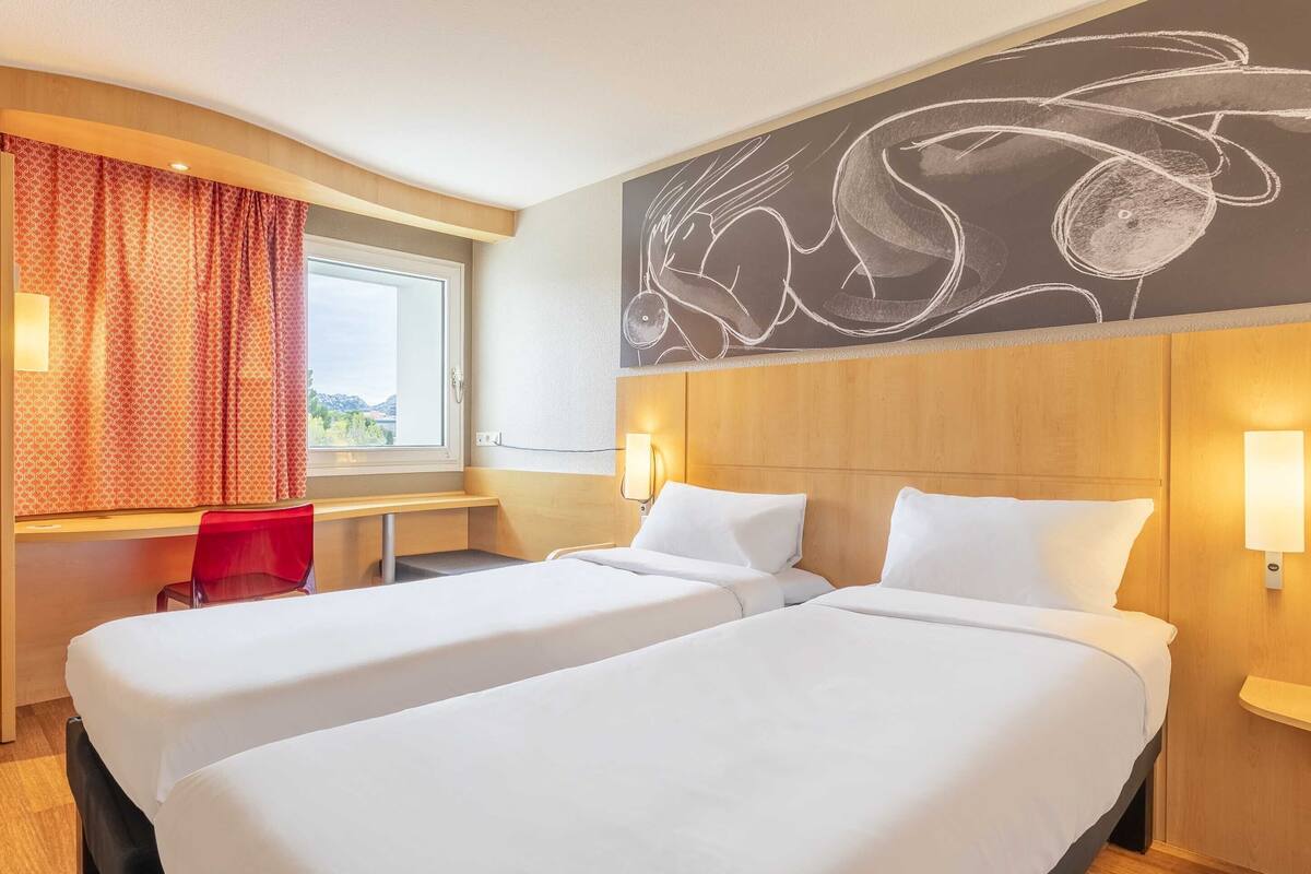 Habitación de hotel con dos camas, un escritorio, una silla y un cuadro abstracto grande en la pared.
