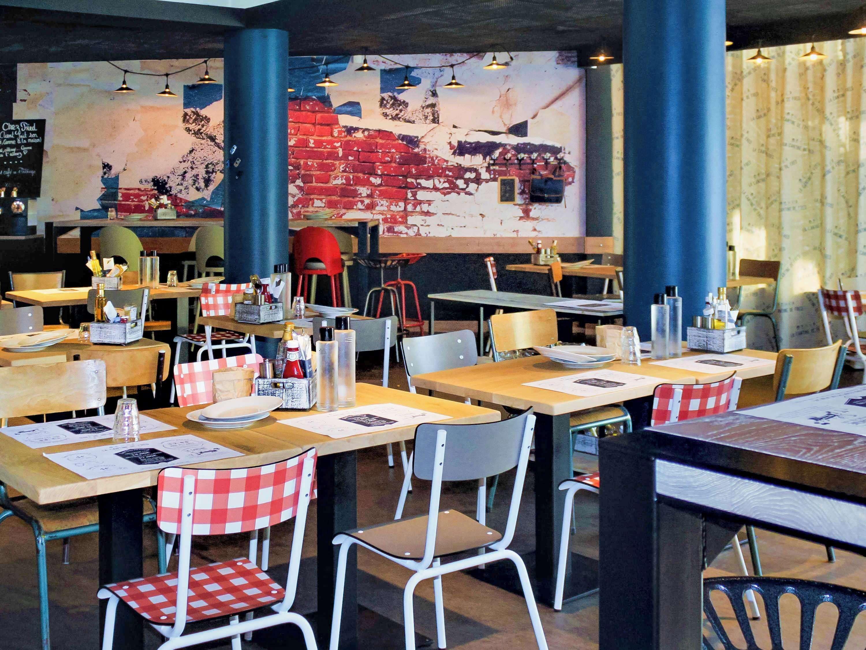 A restaurant interior with multiple tables and chairs, some with red and white checkered tablecloths.