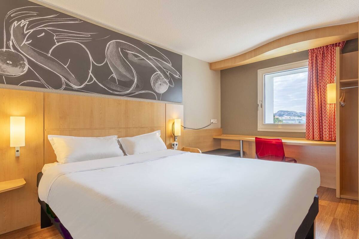 Habitación de hotel con una cama grande, un escritorio, una silla y vistas al exterior.