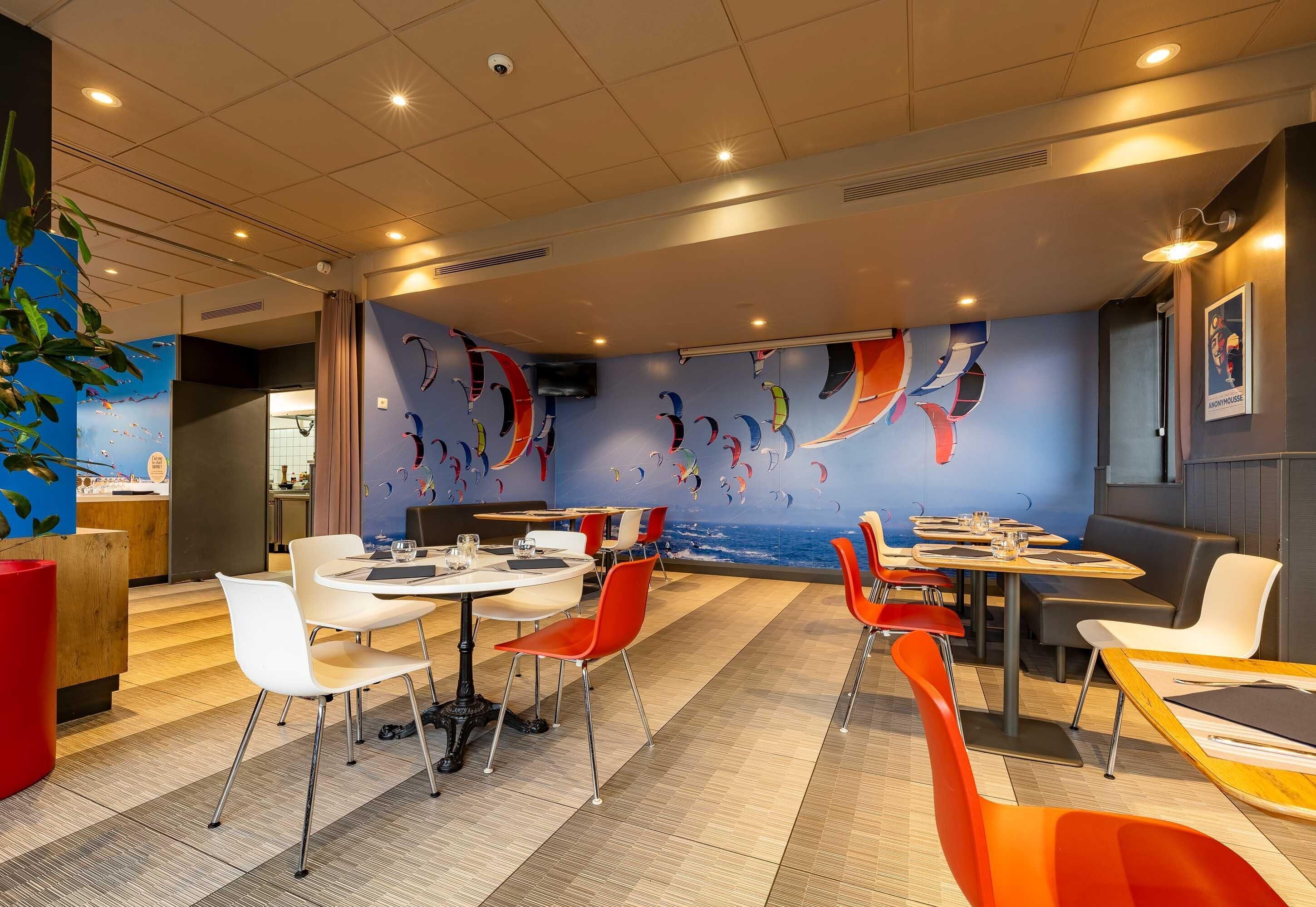 Un restaurante con un mural náutico, varias mesas y sillas para comer, y vistas al área de la cocina.