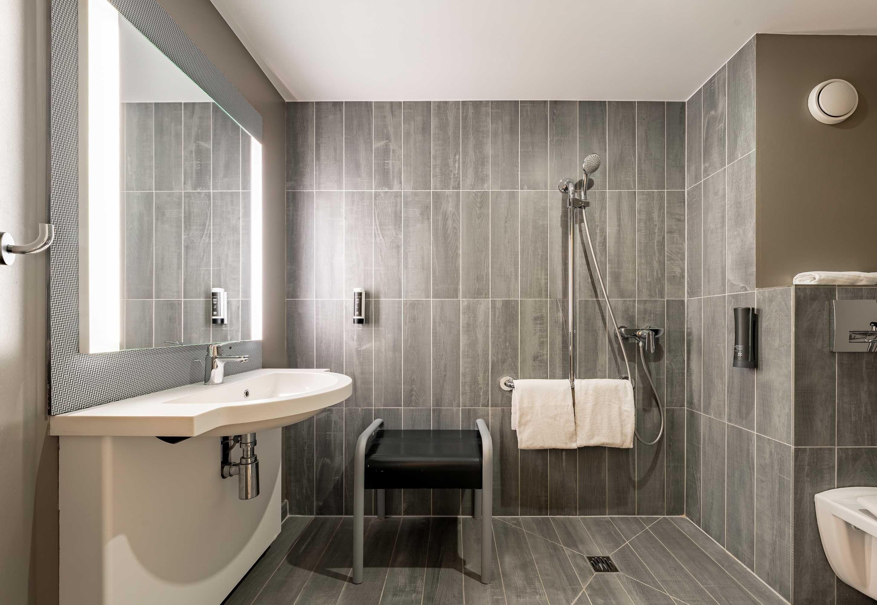 A modern bathroom with a sink, mirror, shower, and towel rack.