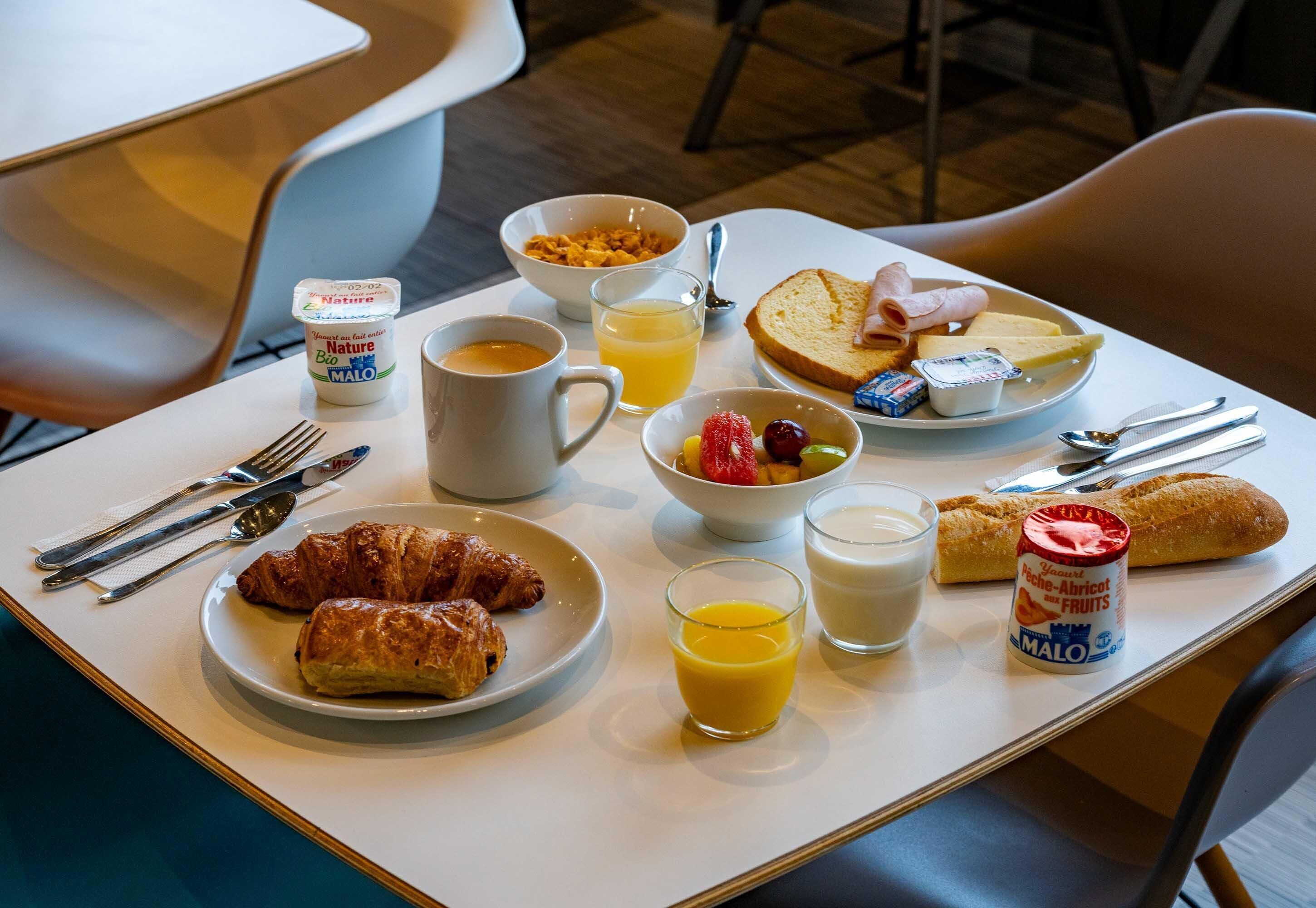 A breakfast table with croissants, fruit, yogurt, and juice.