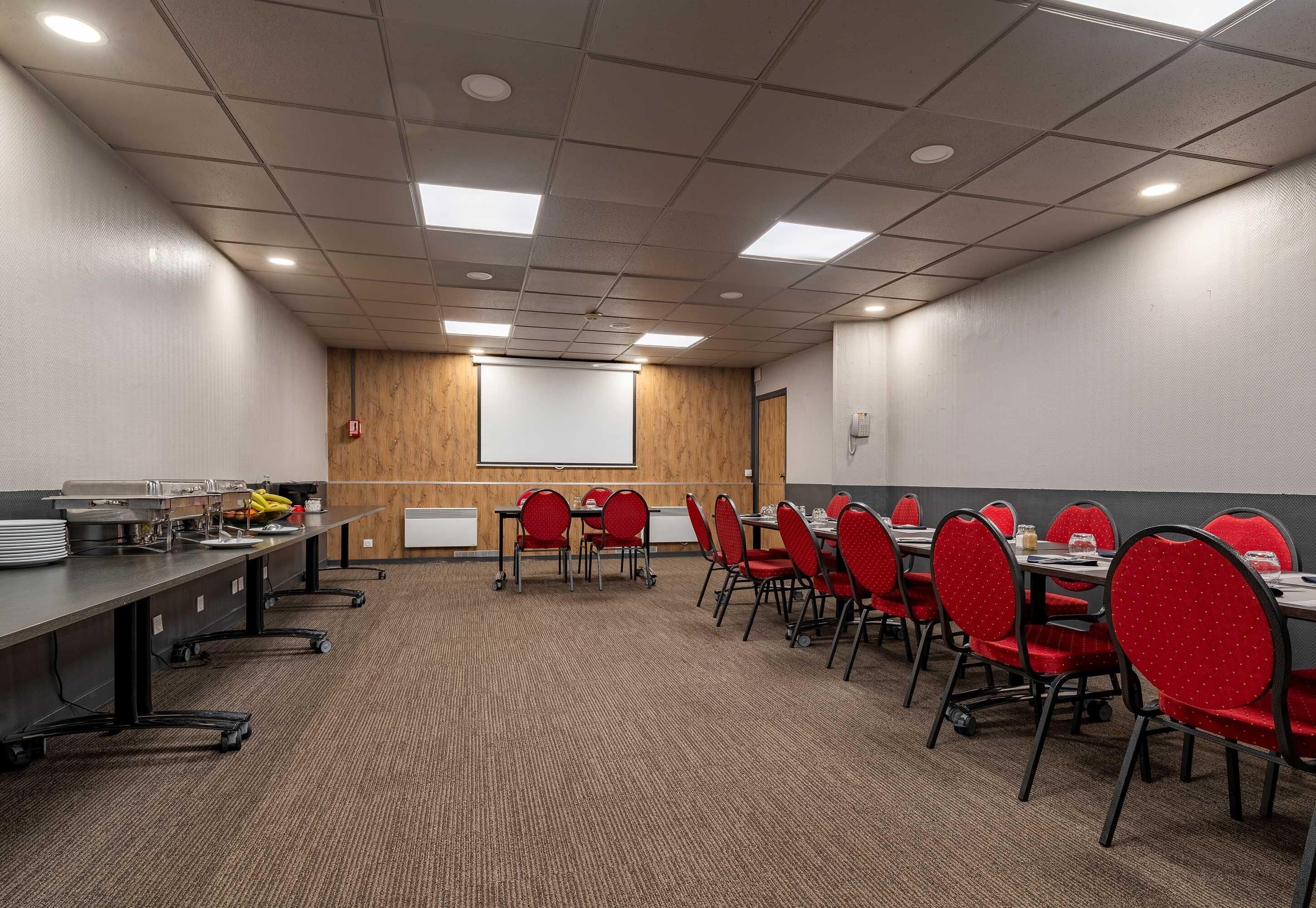 Une salle de conférence avec une longue table, des chaises rouges, un écran de projection et un tableau blanc.