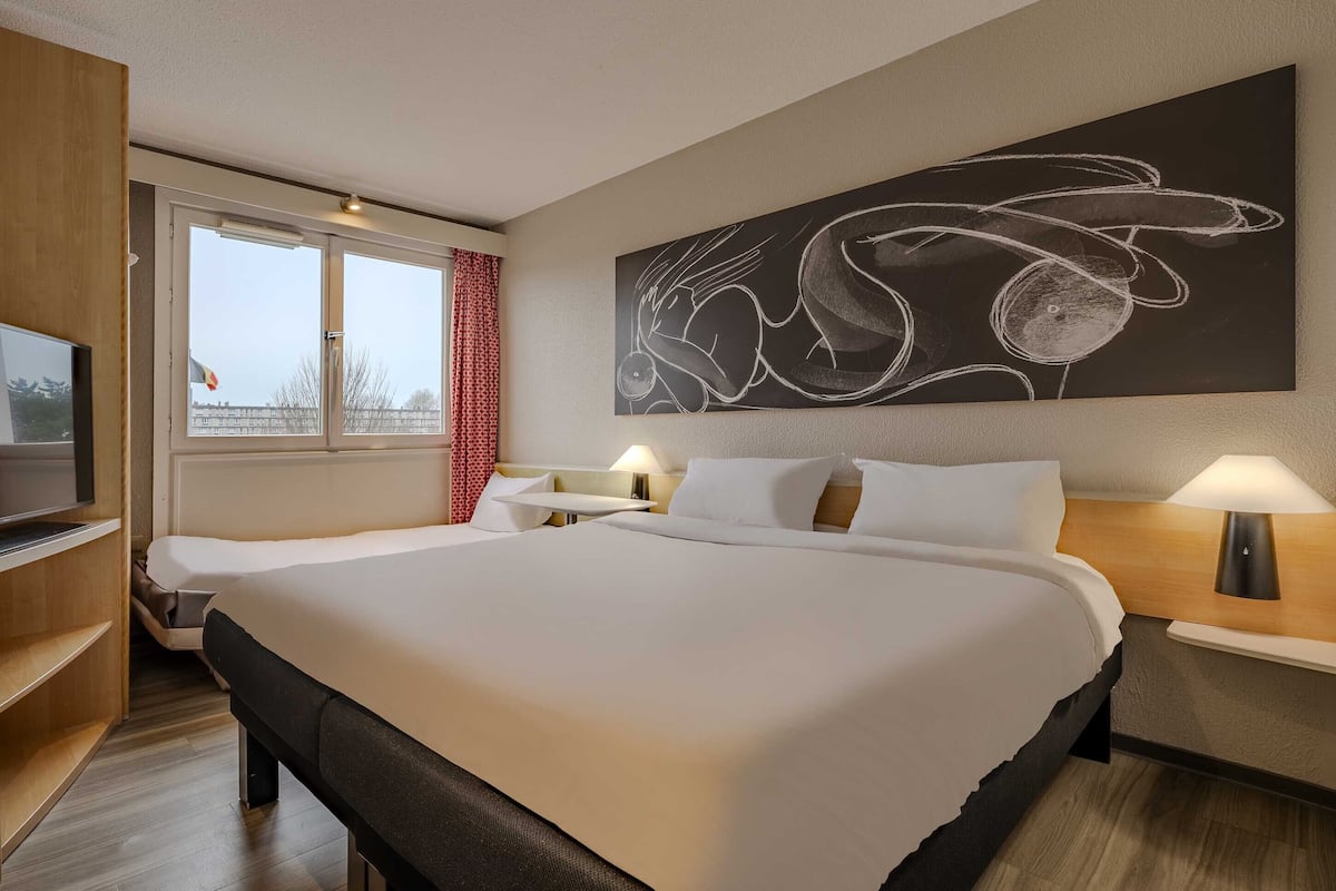 A hotel room with a large bed, a TV, a desk, and a wall-mounted artwork.
