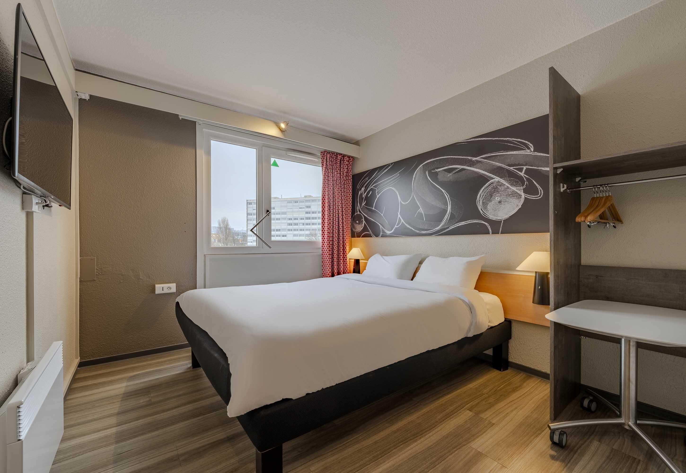 A hotel room with a bed, bedside table, lamp, and a wall-mounted TV.