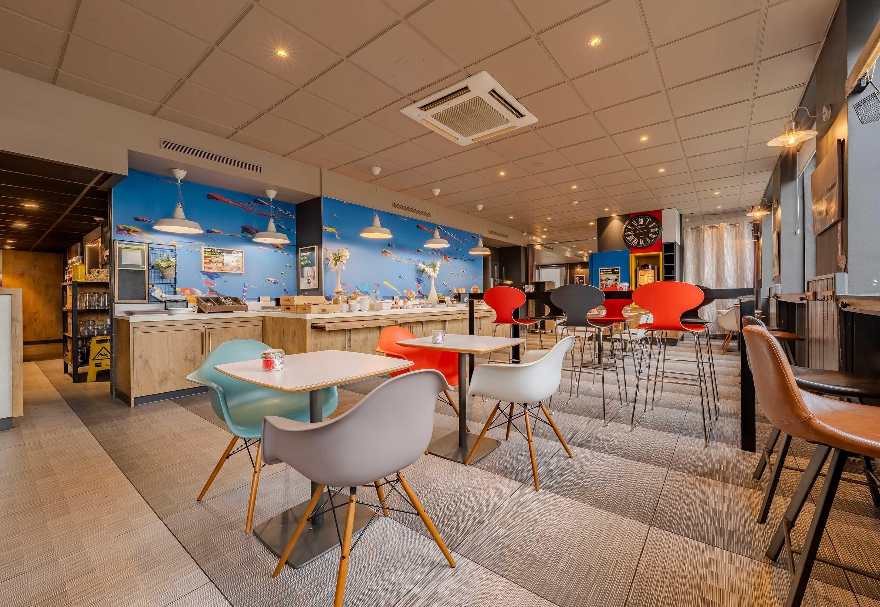 Een modern restaurantinterieur met een blauwe muurschildering, meerdere eettafels en kleurrijke stoelen.
