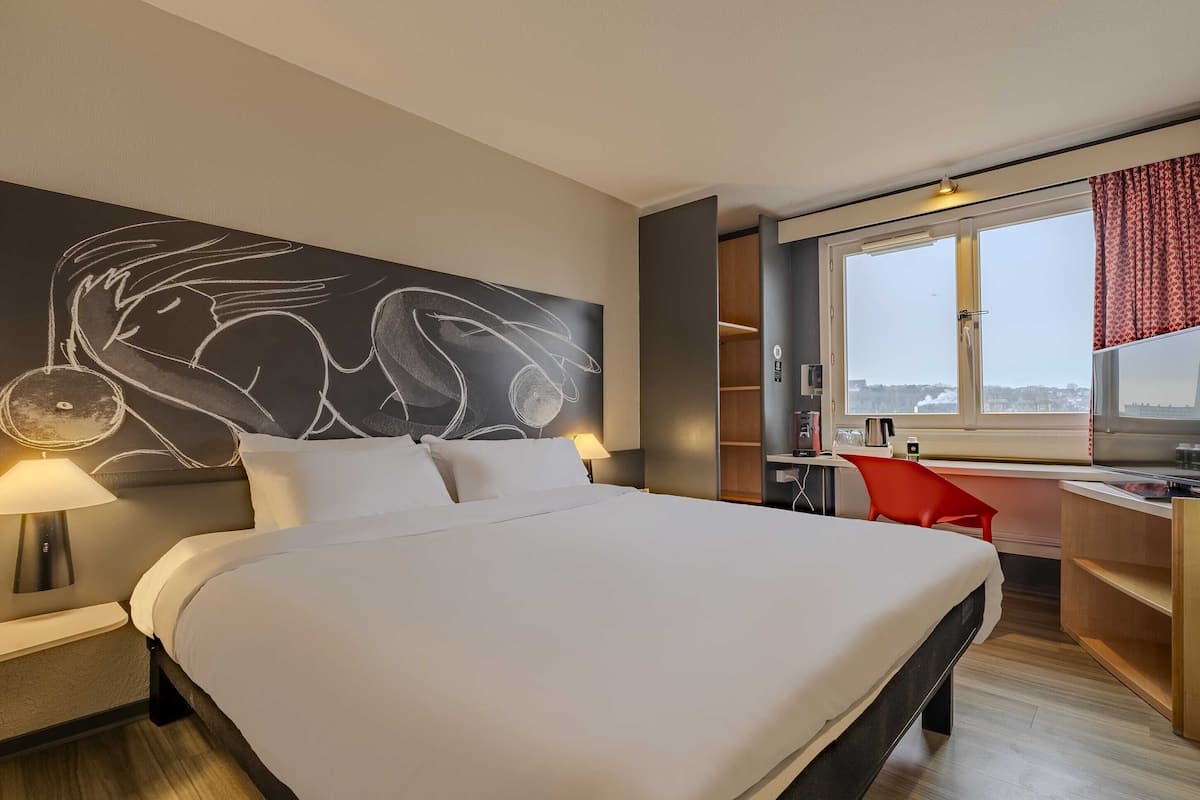 A modern hotel room with a large bed, a desk, and a view of the city.